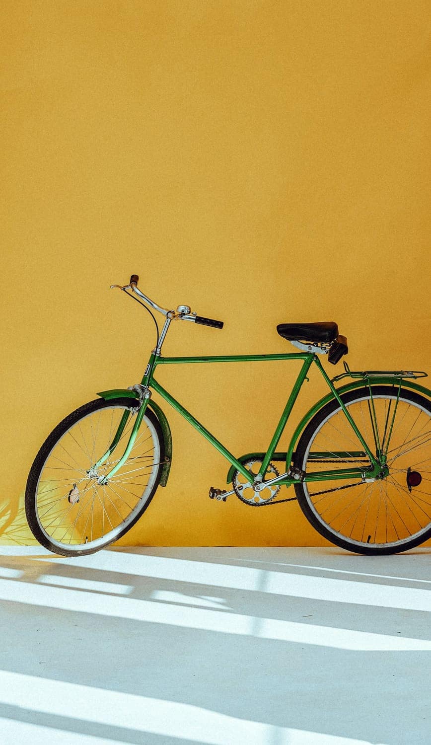 A green bicycle parked against a yellow wall