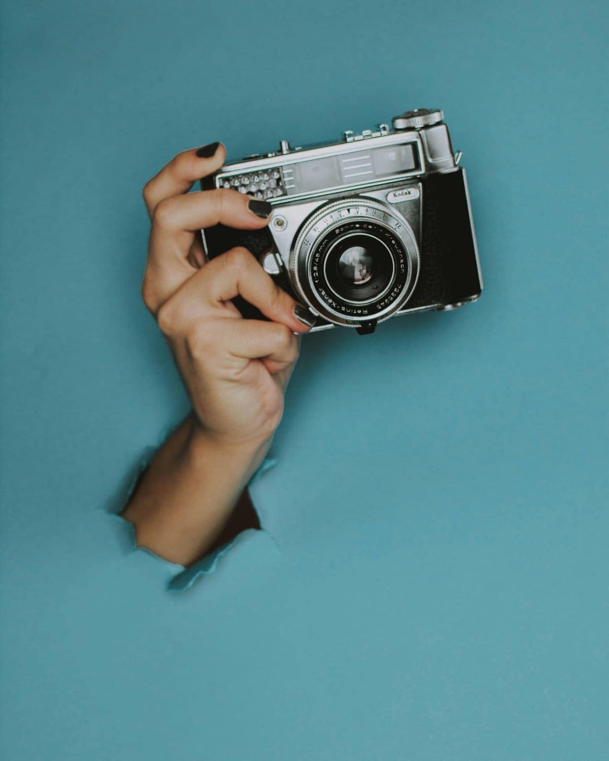 A hand holding a vintage film camera against a teal wall