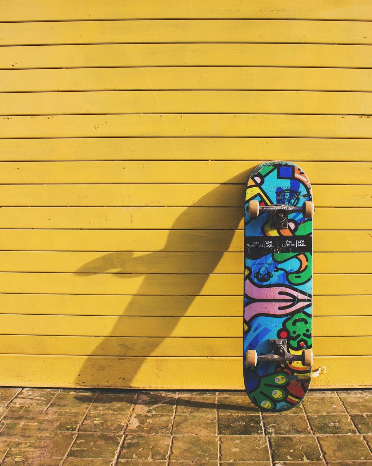 A colourful skateboard leaning against a yellow wall