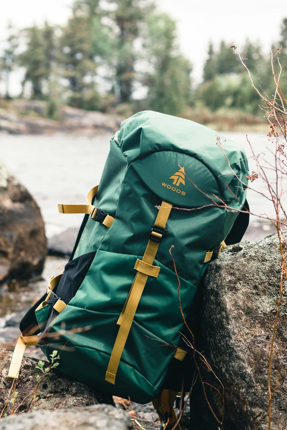 A green hiking backpack resting on a rock by a river