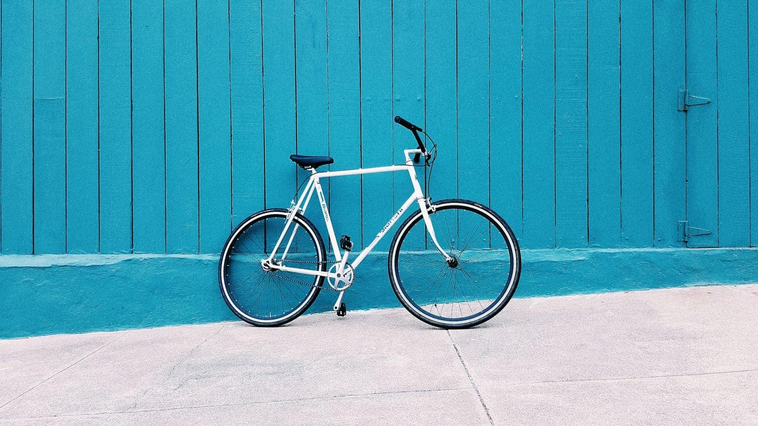 White road bike leaning on a teal wooden wall