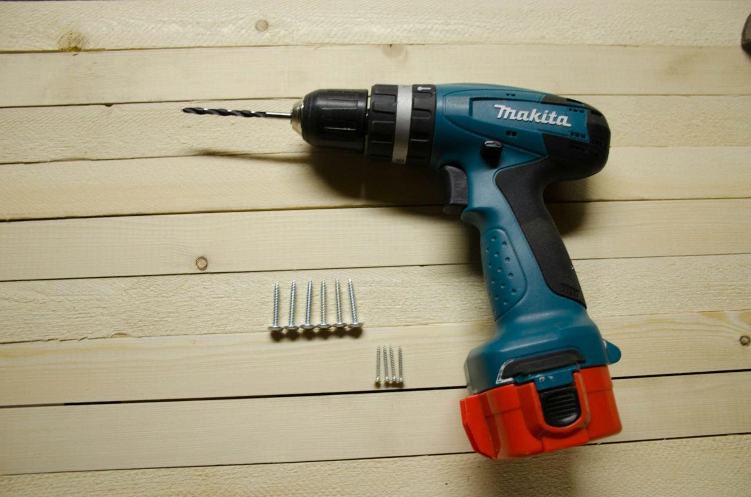 Cordless drill laid on light wood with screws