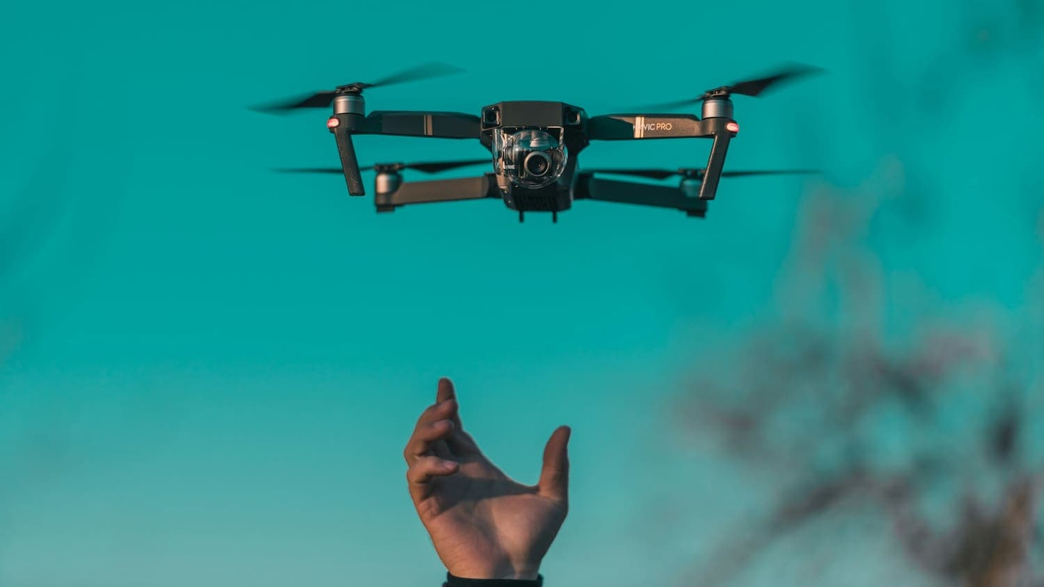 Small camera drone hovering against a teal sky