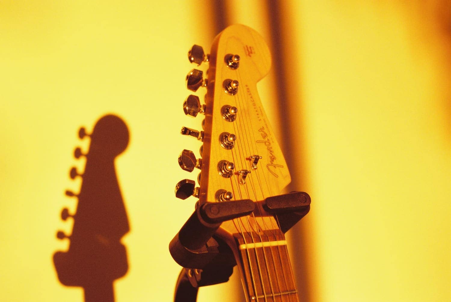 An electric guitar headstock casting a shadow on a warm yellow wall