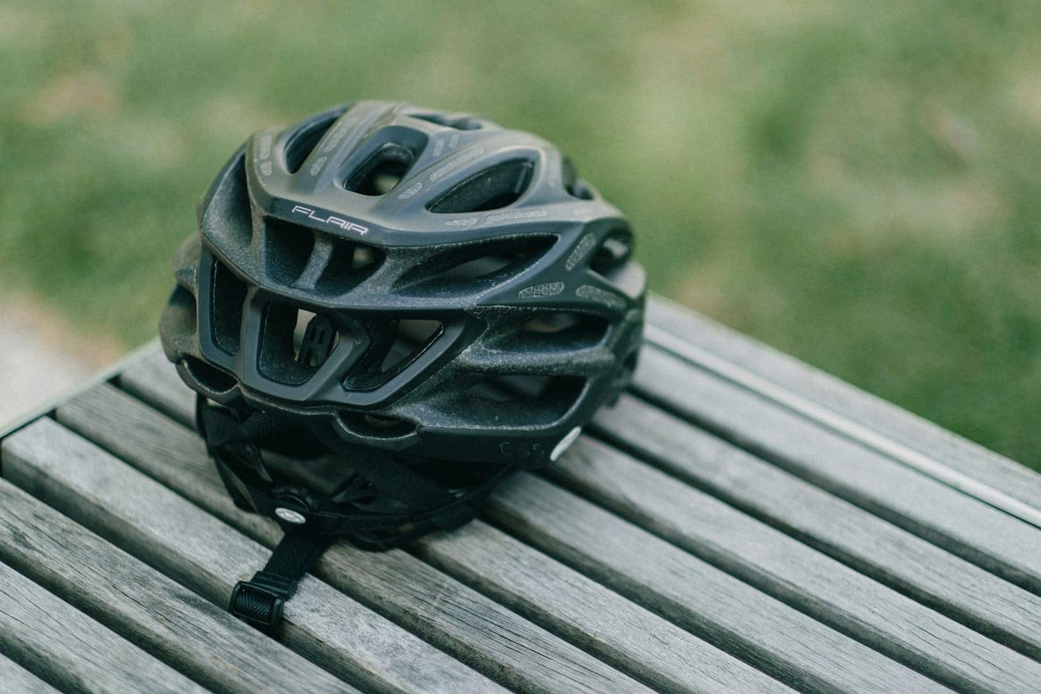 Cycling helmet on a wooden bench with green foliage behind