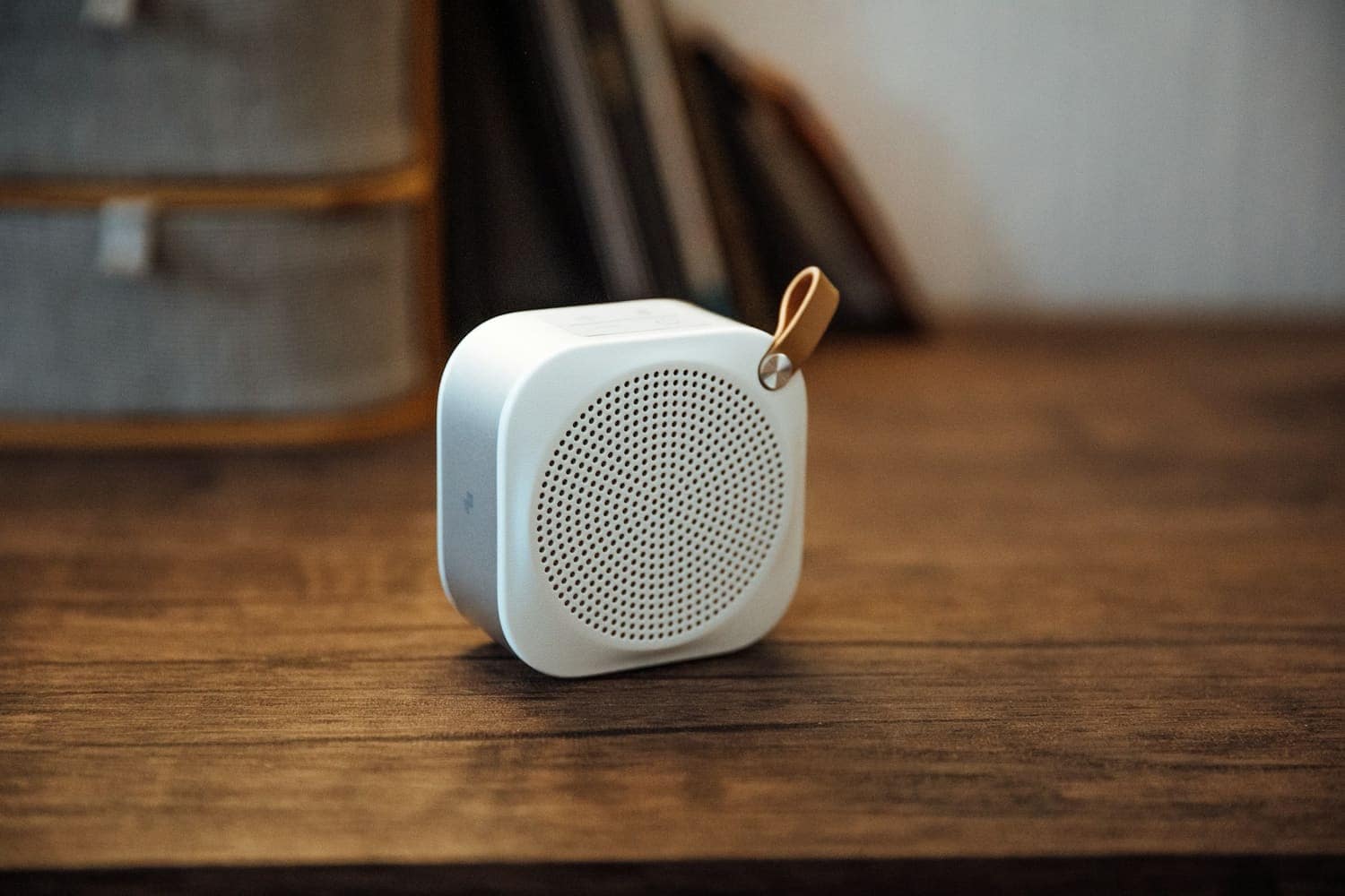 Small white speaker with a leather strap on a wooden table