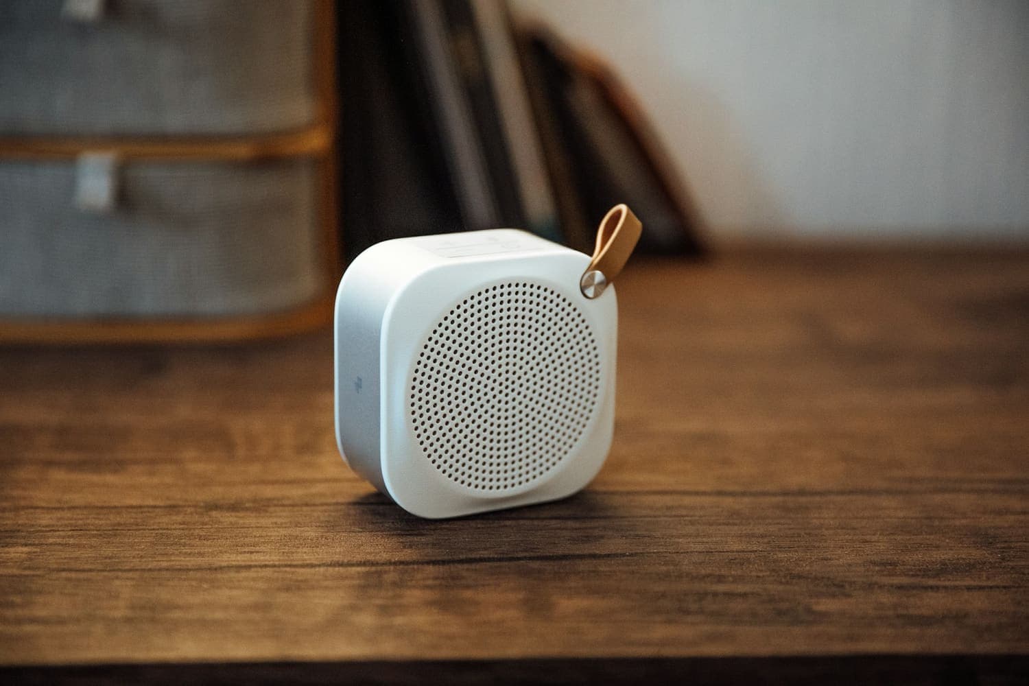 Small white speaker with a leather strap on a wooden table