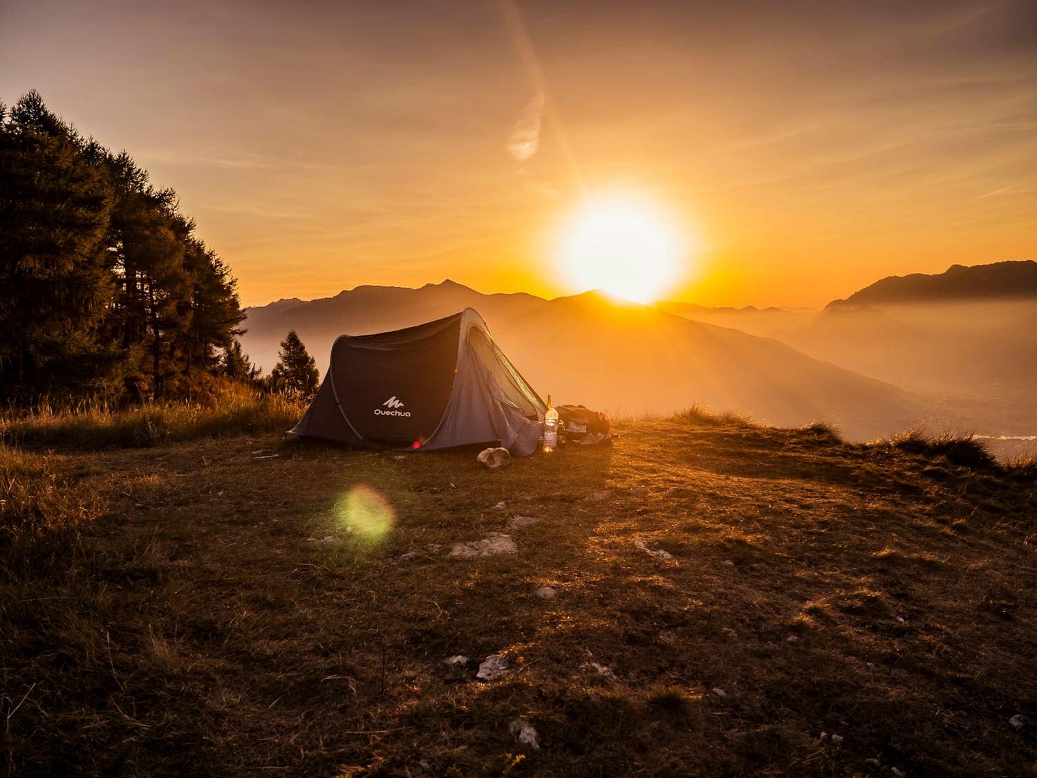 A tent on a mountain top with the sun setting behind it